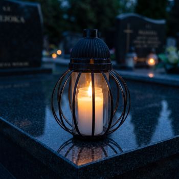 Znicz lampion czarny, kula z drutów zapalony na nagrobku nocą