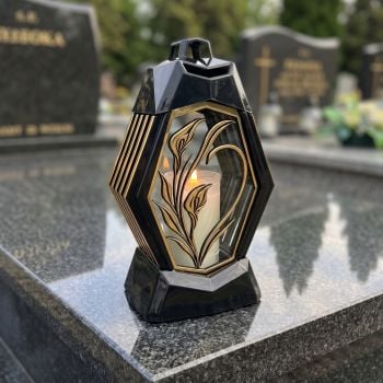 Znicz lampion czarno-złoty z kalią na nagrobku w słoneczny dzień