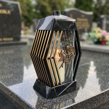 Znicz lampion czarno-złoty z różą na nagrobku w słoneczny dzień