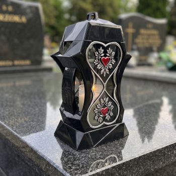 Znicz kapliczka czarno-srebrny z czerwonymi sercami na nagrobku w słoneczny dzień