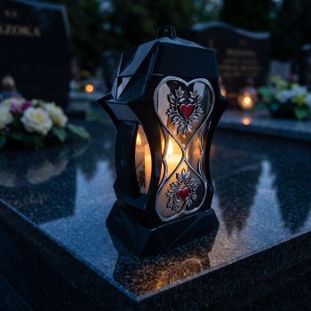 Znicz kapliczka czarno-srebrny z czerwonymi sercami zapalony na nagrobku nocą