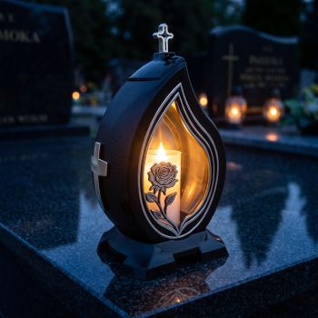 Znicz kapliczka czarno-srebrny z różą i krzyżem zapalony na nagrobku nocą