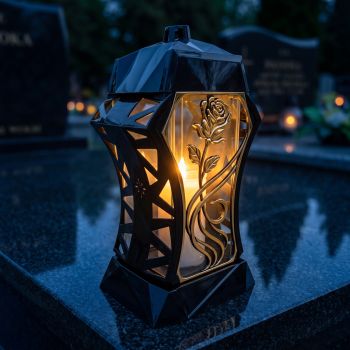 Znicz kapliczka czarno-złoty ze złotą różą pnącą zapalony na nagrobku nocą