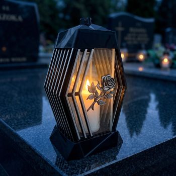 Znicz kapliczka czarno-srebrny z różą zapalony na nagrobku nocą