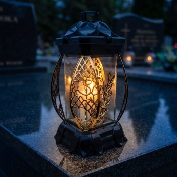 Znicz kapliczka czarno-złoty ze złotą lilią zapalony na nagrobku nocą