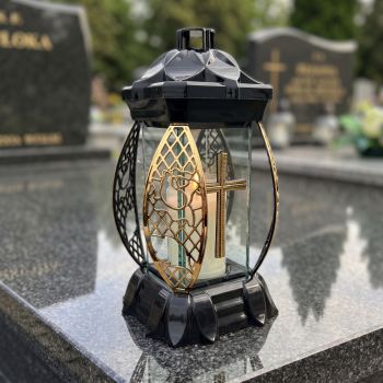 Znicz lampion czarno-złoty ze złotym krzyżem na nagrobku w słoneczny dzień