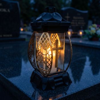 Znicz lampion czarno-złoty ze złotym krzyżem zapalony na nagrobku nocą