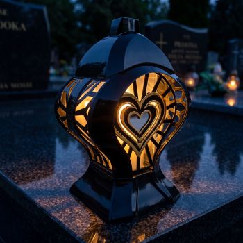 Znicz kapliczka czarno-złoty ze złotym sercem zapalony na nagrobku nocą