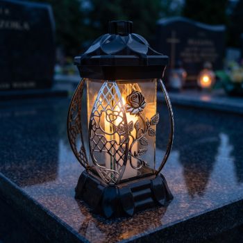 Znicz kapliczka czarno-srebrny ze srebrną różą pnącą zapalony na nagrobku nocą