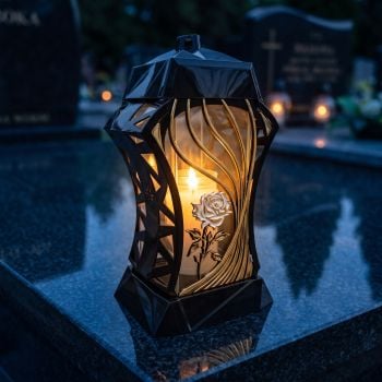 Znicz szklany czarno-złoty z różą perłową zapalony na nagrobku nocą