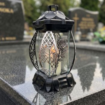 Znicz lampion czarno-srebrny ze srebrną różą na nagrobku w słoneczny dzień