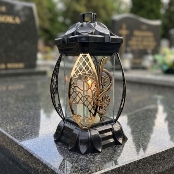 Znicz lampion czarno-złoty ze złotą monsterą na nagrobku w słoneczny dzień