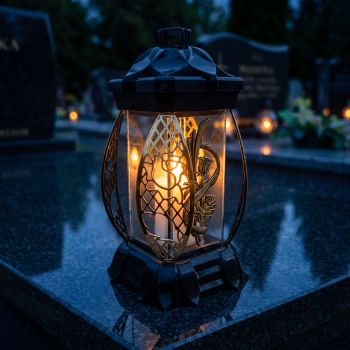 Znicz lampion czarno-złoty ze złotą monsterą zapalony na nagrobku nocą