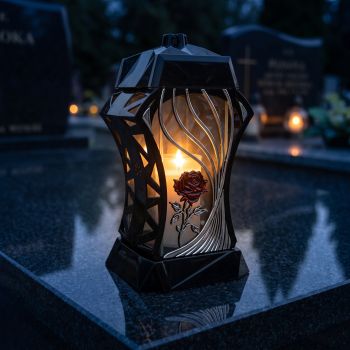 Znicz kapliczka czarno-srebrny z czerwoną różą zapalony na nagrobku nocą