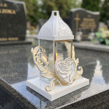 Znicz kapliczka biało-złoty z różą w sercu na nagrobku w słoneczny dzień