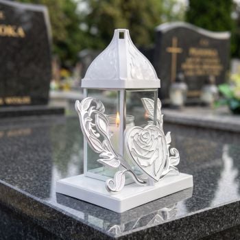 Znicz kapliczka biało-srebrny z różą w sercu na nagrobku w słoneczny dzień