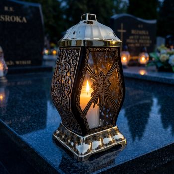 Znicz kapliczka czarno-złoty z krzyżem zapalony na nagrobku nocą