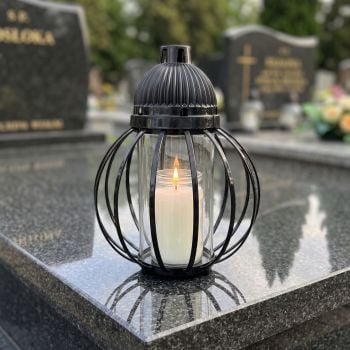 Znicz lampion czarny, kula z drutów na nagrobku w słoneczny dzień